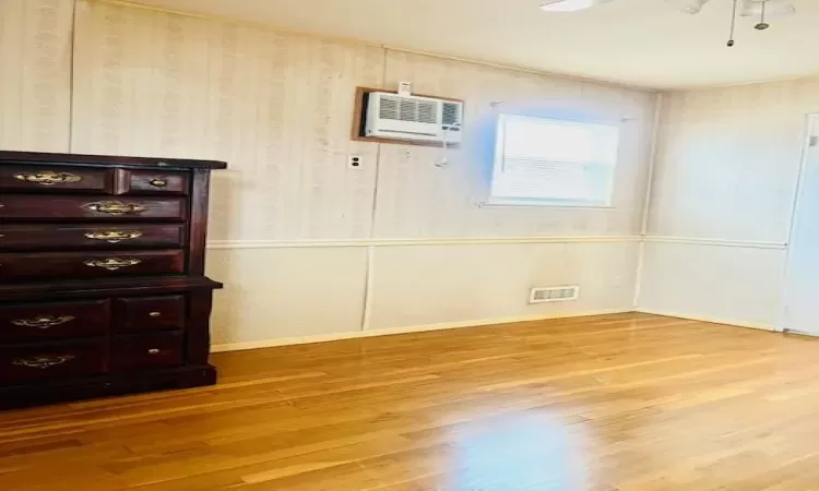 Primary Bedroom room with light haedwood flooring, an AC wall unit, and ceiling fan