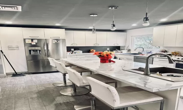 Kitchen featuring white cabinetry, a kitchen breakfast bar, light hardwood / wood-style flooring, stainless steel fridge, and decorative light fixtures