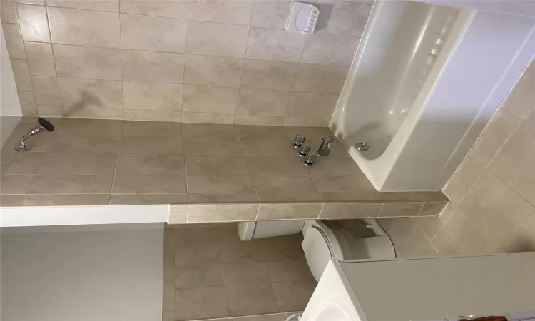 Full bathroom featuring vanity, tile patterned flooring, tiled shower / bath combo, toilet, and tile walls