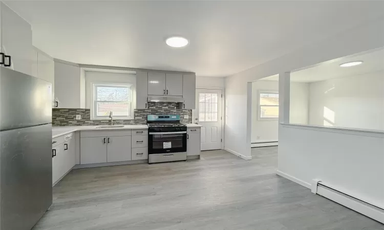 Kitchen with stainless steel appliances, baseboard heating, light hardwood / wood-style floors, and sink