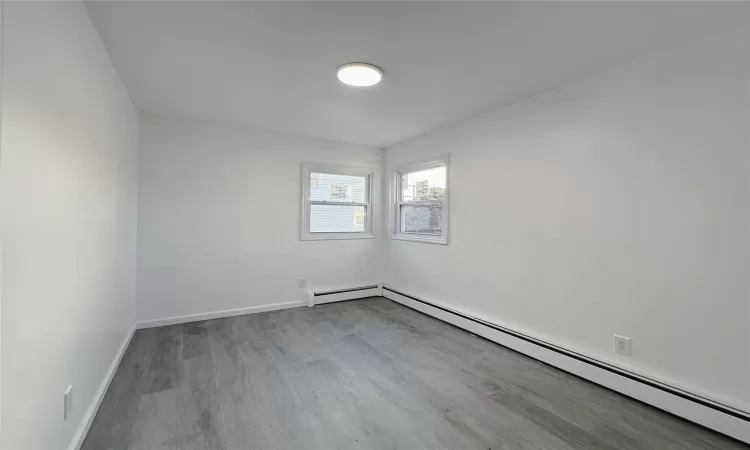 Empty room with light wood-type flooring and a baseboard heating unit