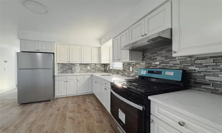 Kitchen with sink, light hardwood / wood-style flooring, backsplash, white cabinets, and appliances with stainless steel finishes