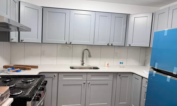 Kitchen with gray cabinetry, refrigerator, sink, and range hood