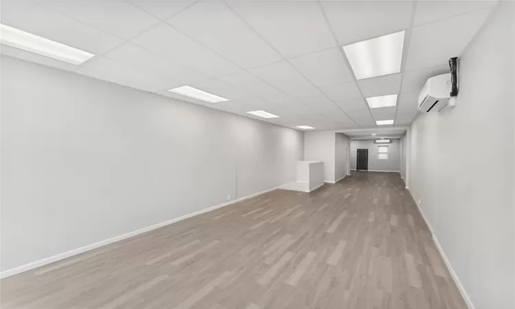 Basement with a paneled ceiling, light wood-type flooring, and an AC wall unit