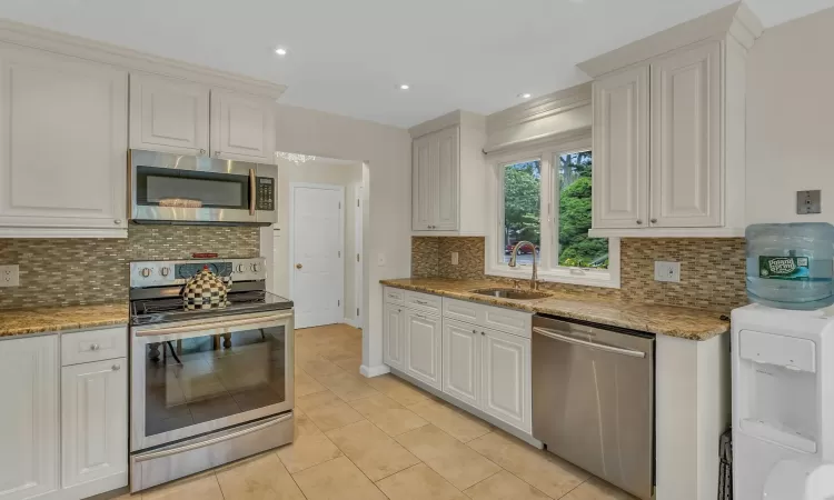 Kitchen with appliances with stainless steel finishes, tasteful backsplash, white cabinetry, and sink