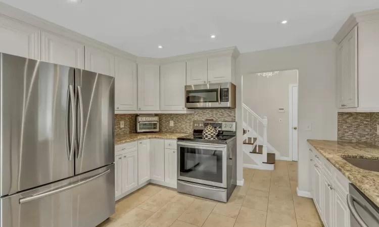 Kitchen featuring white cabinets, appliances with stainless steel finishes, decorative backsplash, and light stone countertops