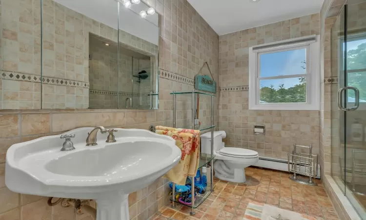 Bathroom with a shower with door, sink, toilet, tile walls, and a baseboard radiator