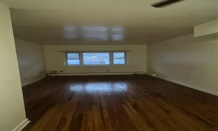 Empty room featuring dark wood-type flooring and a baseboard radiator