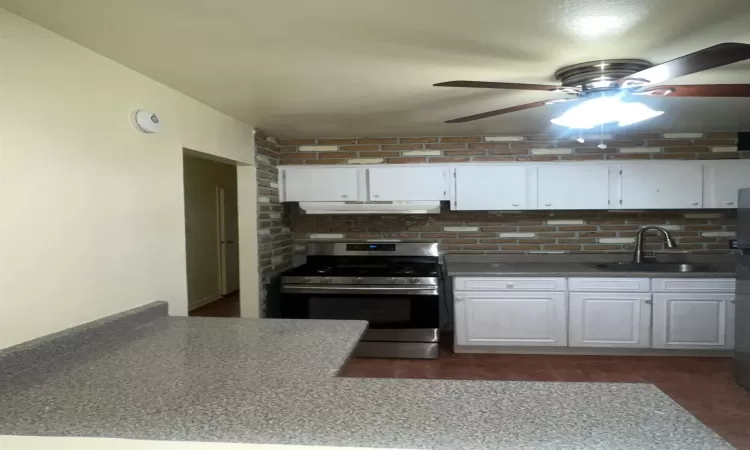 Kitchen with white cabinets, stainless steel range with gas cooktop, ceiling fan, and sink