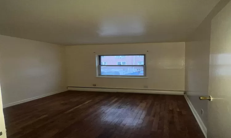 Empty room with baseboard heating, dark wood-type flooring, and vaulted ceiling