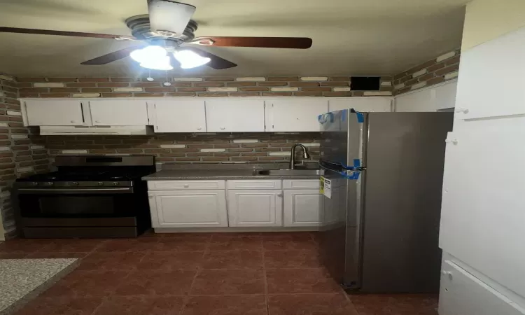 Kitchen featuring white cabinetry, sink, ceiling fan, dark tile patterned flooring, and appliances with stainless steel finishes