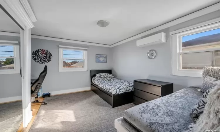 Carpeted bedroom with a wall unit AC, multiple windows, and ornamental molding