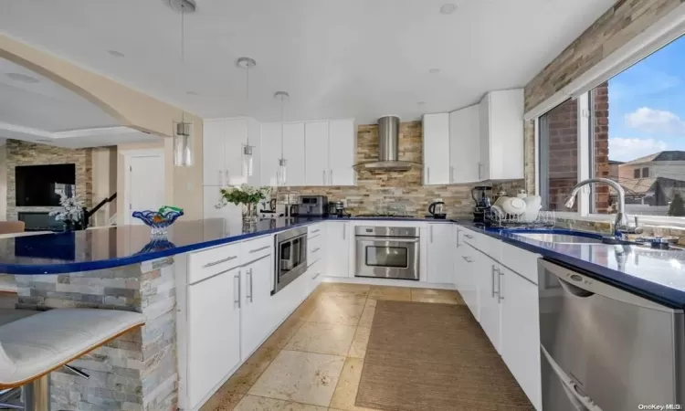 Kitchen with stainless steel appliances, white cabinetry, hanging light fixtures, and wall chimney exhaust hood