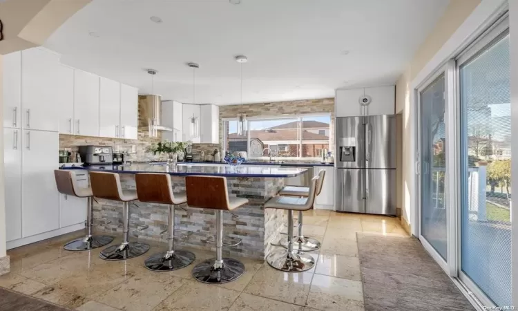 Kitchen featuring white cabinets, a kitchen breakfast bar, stainless steel fridge, and decorative light fixtures