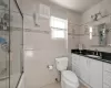 Full bathroom featuring vanity, shower / bath combination with glass door, tile walls, tile patterned flooring, and toilet