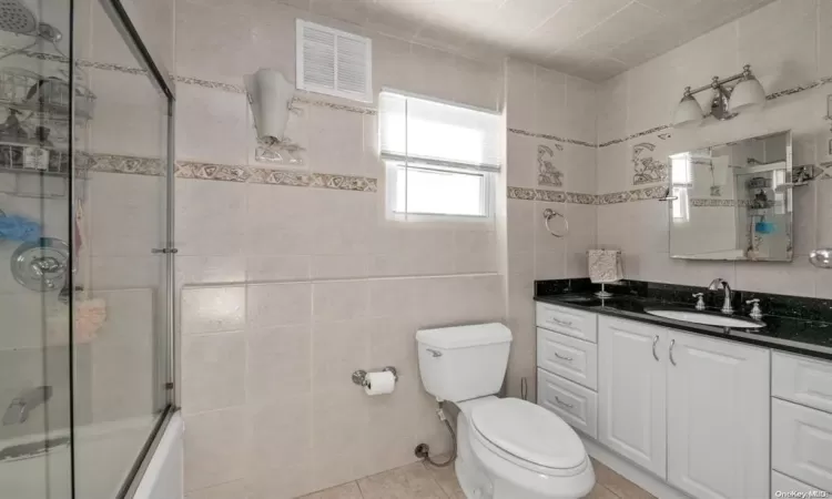 Full bathroom featuring vanity, shower / bath combination with glass door, tile walls, tile patterned flooring, and toilet