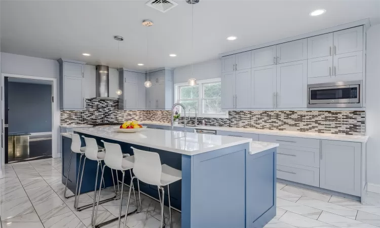 Kitchen with pendant lighting, a center island, stainless steel microwave, wall chimney exhaust hood, and a breakfast bar area