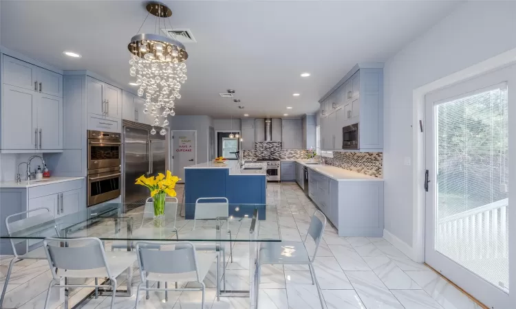 Kitchen with pendant lighting, backsplash, wall chimney range hood, built in appliances, and a kitchen island