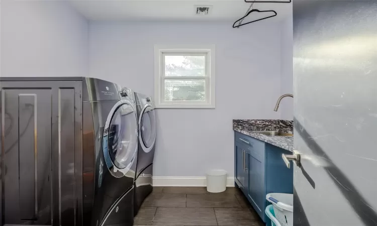 Washroom featuring dark tile patterned flooring, cabinets, sink, and washing machine and clothes dryer