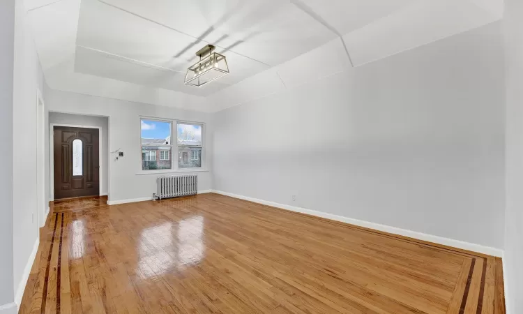 Unfurnished living room featuring wood-type flooring, radiator, and an inviting chandelier