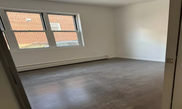 Empty room featuring baseboard heating and dark wood-type flooring