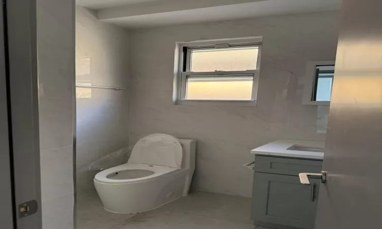 Bathroom with toilet, vanity, tile patterned floors, and tile walls