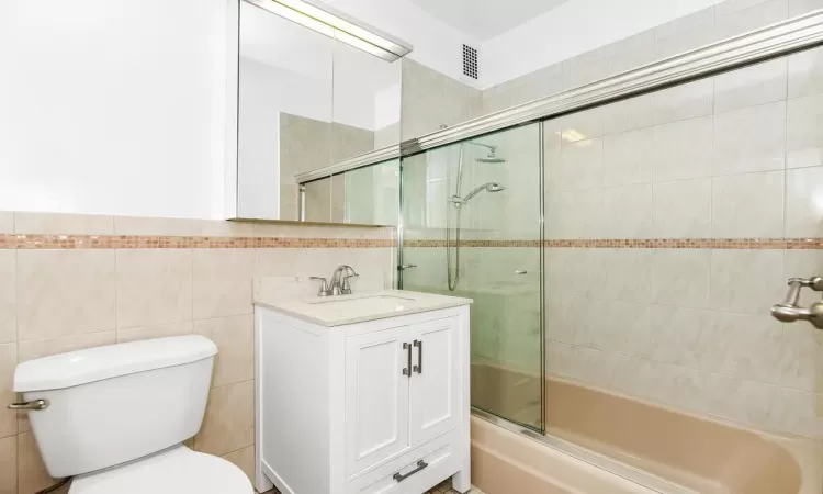 Full bathroom featuring toilet, combined bath / shower with glass door, and tile walls