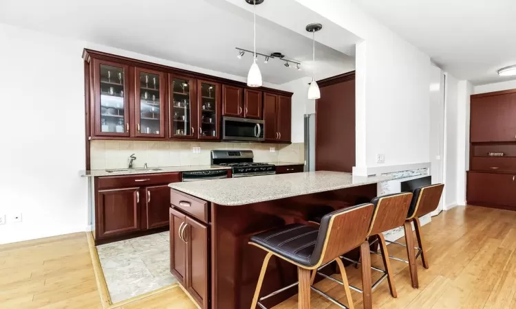 Kitchen with stainless steel appliances, pendant lighting, a breakfast bar area, decorative backsplash, and light wood-type flooring