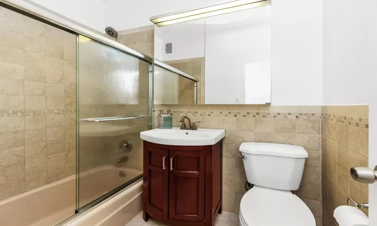 Full bathroom featuring vanity, toilet, shower / bath combination with glass door, and tile walls