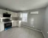 Kitchen with white cabinetry, baseboard heating, a wall mounted AC, and stainless steel gas range