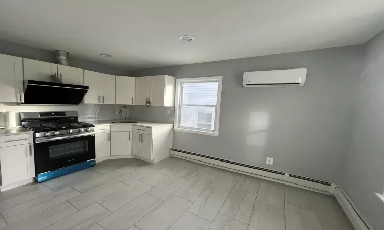 Kitchen with white cabinetry, baseboard heating, a wall mounted AC, and stainless steel gas range