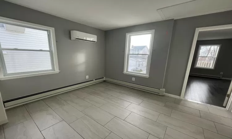 Empty room featuring a wall mounted air conditioner, light hardwood / wood-style floors, and baseboard heating