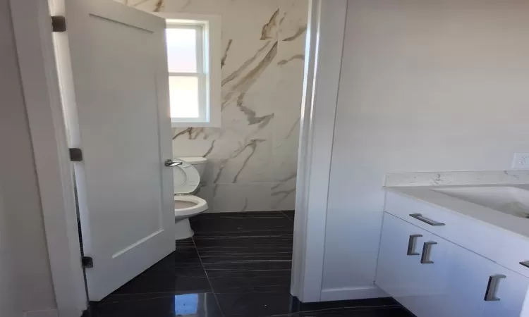 Bathroom with tile patterned flooring, vanity, toilet, and tile walls