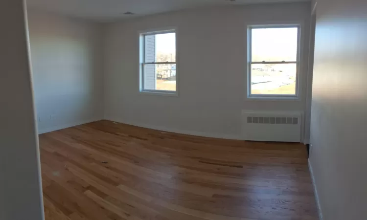 Empty room featuring light hardwood / wood-style floors, plenty of natural light, and radiator