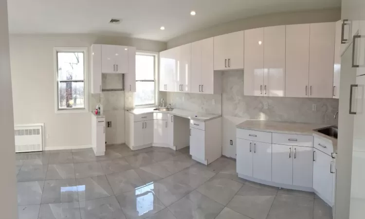 Kitchen with white cabinets, radiator heating unit, sink, and tasteful backsplash