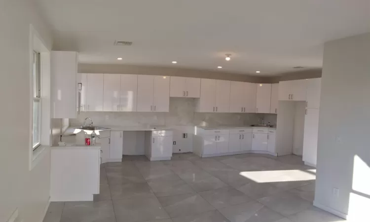 Kitchen with decorative backsplash, white cabinetry, and sink