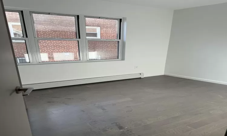 Empty room with dark hardwood / wood-style flooring and a baseboard radiator