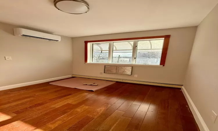 Spare room featuring baseboard heating, a wall mounted AC, and dark hardwood / wood-style flooring