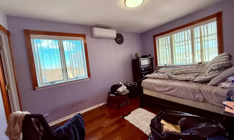 Bedroom with dark hardwood / wood-style flooring, a wall unit AC, and multiple windows