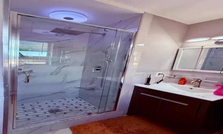 Bathroom featuring vanity, tile walls, and a shower with shower door