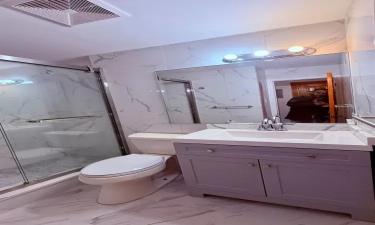 Bathroom featuring vanity, toilet, and a shower with door