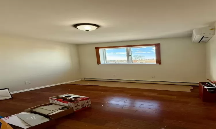 Spare room featuring an AC wall unit, dark hardwood / wood-style floors, and a baseboard heating unit