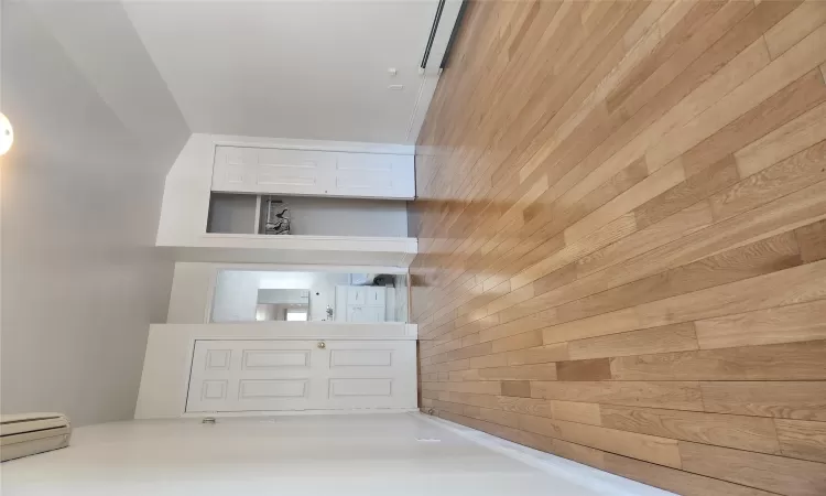 Unfurnished bedroom featuring an AC wall unit, a baseboard radiator, and light wood-type flooring