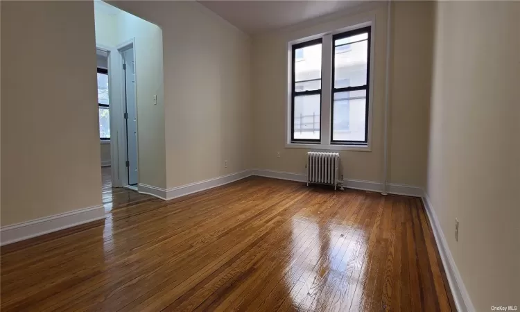 Unfurnished room featuring hardwood / wood-style flooring, radiator heating unit, and crown molding