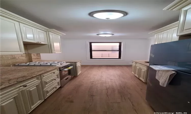 Kitchen with tasteful backsplash, black fridge, dark hardwood / wood-style flooring, and light stone countertops