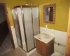 Bathroom featuring vanity, a shower with shower door, tile walls, and toilet