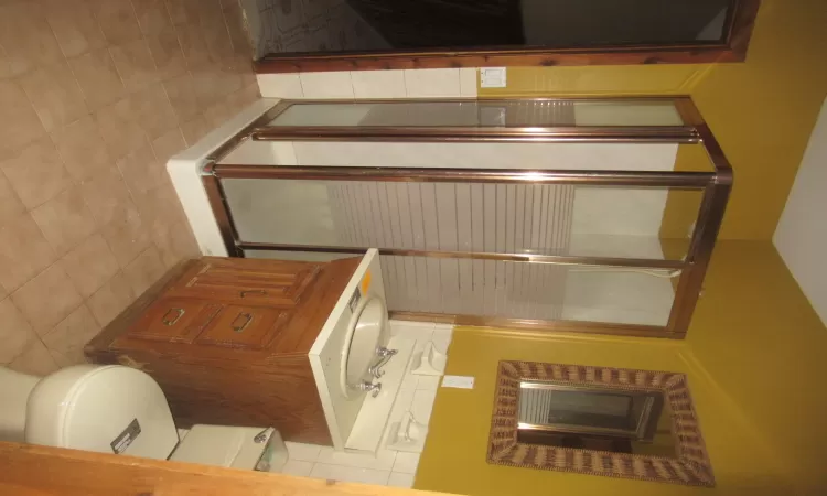 Bathroom featuring tile patterned floors, vanity, tile walls, toilet, and a shower with shower door