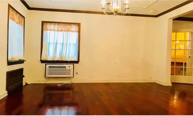 Spare room with a wall mounted AC, crown molding, a notable chandelier, and hardwood / wood-style flooring