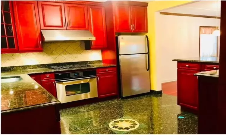 Kitchen with appliances with stainless steel finishes, backsplash, sink, pendant lighting, and dark stone countertops