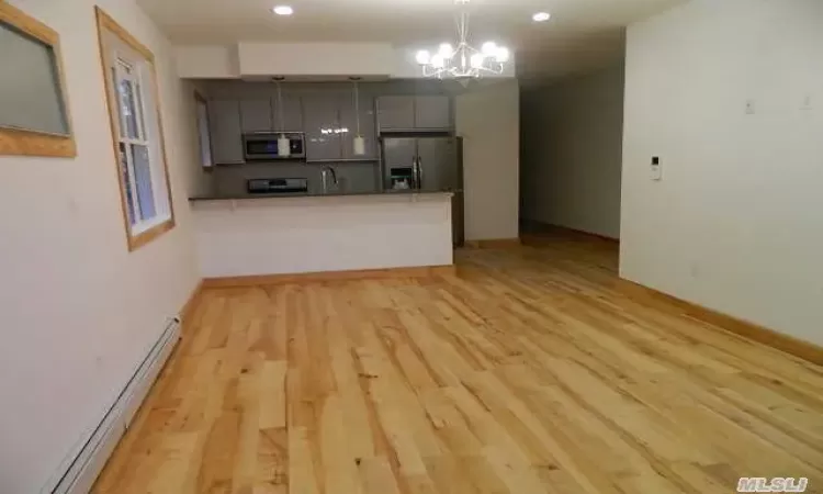 Kitchen with kitchen peninsula, appliances with stainless steel finishes, gray cabinetry, baseboard heating, and light hardwood / wood-style flooring